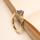 Blue sapphire engagement ring with an oval-cut sapphire accented by diamond-set and a polished yellow gold band.