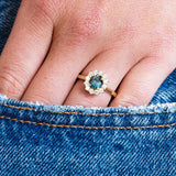 Teal sapphire ring worn on hand with denim pocket detail.