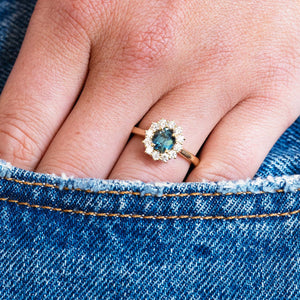 Teal sapphire ring worn on hand with denim pocket detail.