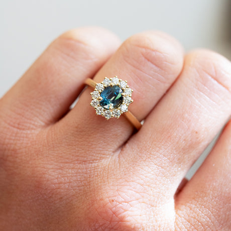 Oval cut teal sapphire ring with diamond halo showing rich blue green tone.