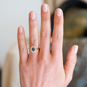 Teal sapphire cluster ring worn on hand with natural manicure.