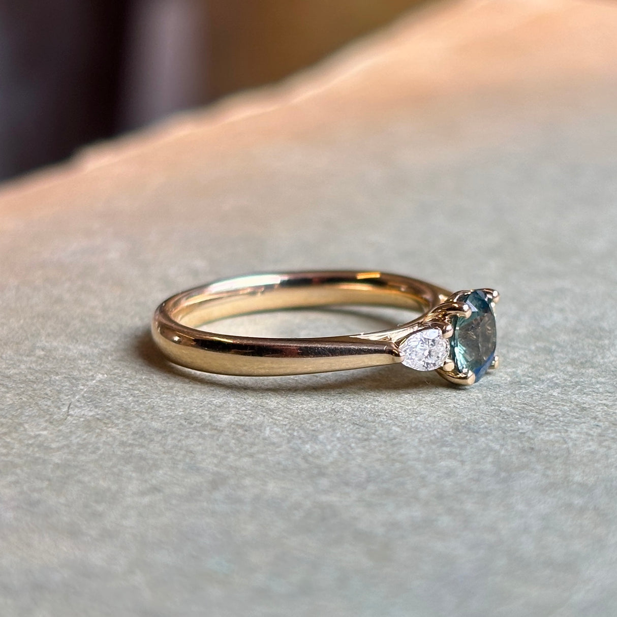 Yellow gold three-stone engagement ring with oval Sri Lankan green sapphire centre and diamond side stones.