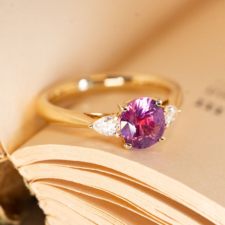 Oval-cut pink-red sapphire engagement ring with pear-cut diamond accents and an elegant yellow gold band.