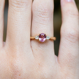 Pink sapphire and diamond three-stone engagement ring worn on finger with pear-shaped diamond side stones.
