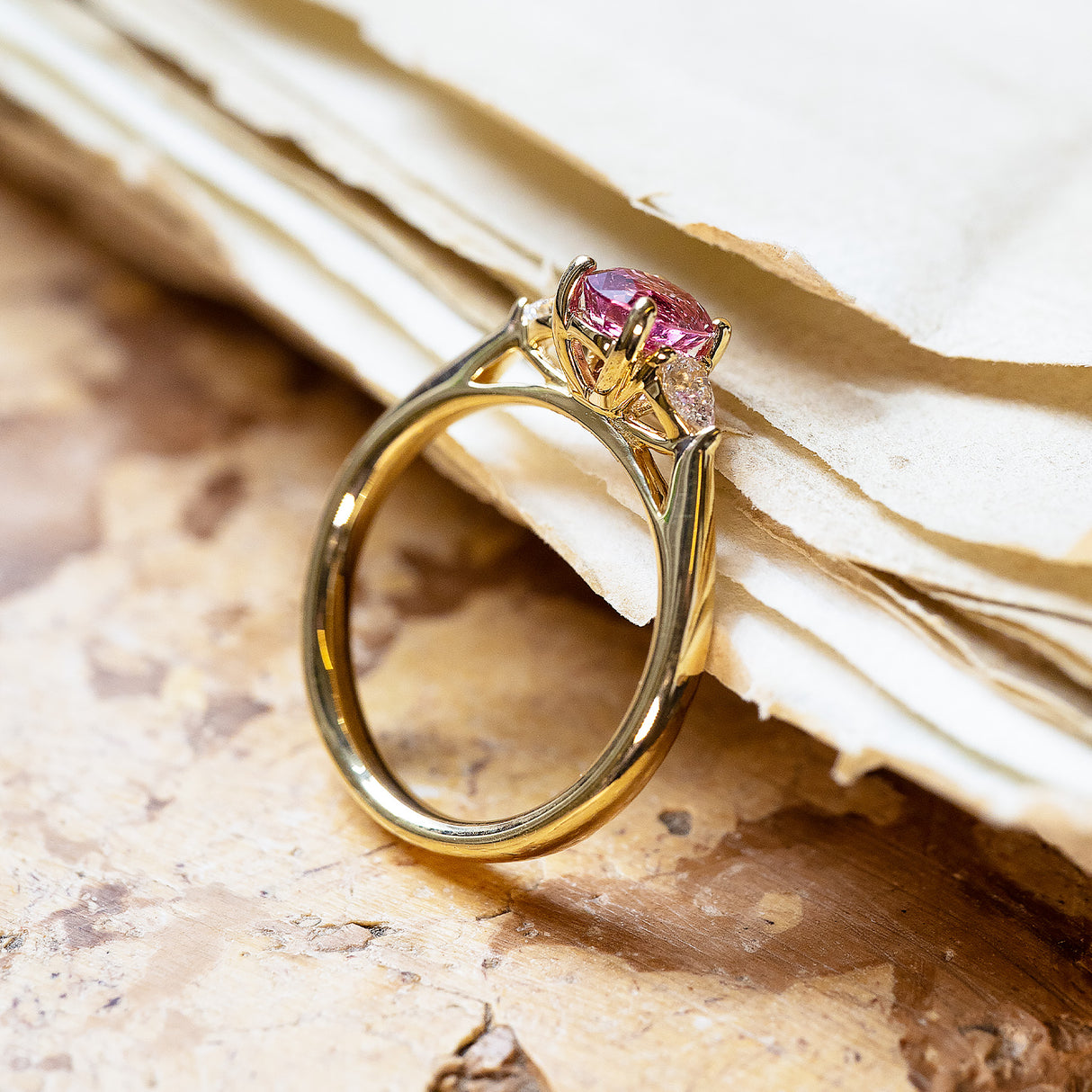 Pink sapphire and diamond three-stone engagement ring with elevated setting and polished gold band.