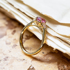 Pink sapphire and diamond three-stone engagement ring with elevated setting and polished gold band.