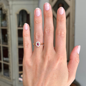 Antique-inspired yellow gold ruby and diamond cluster ring worn on hand, featuring an oval-cut ruby centre stone framed by sparkling diamonds in natural light.