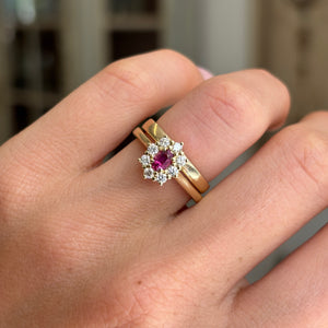 Antique-inspired yellow gold ruby cluster ring worn on hand, featuring an oval-cut ruby surrounded by diamonds, photographed to highlight the classic cluster design and fine craftsmanship.