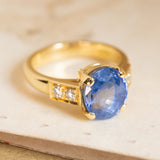 Vintage sapphire engagement ring set with an oval-cut blue sapphire and sparkling diamond accents in a polished yellow gold setting.
