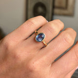 Close-up of an antique-inspired yellow gold sapphire solitaire ring showcasing an oval-cut slate blue sapphire in a polished rub-over setting against a warm interior backdrop.