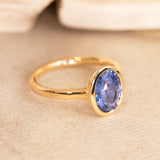 Oval-cut slate blue sapphire solitaire ring in a yellow gold rub-over setting with a refined, antique-inspired silhouette.