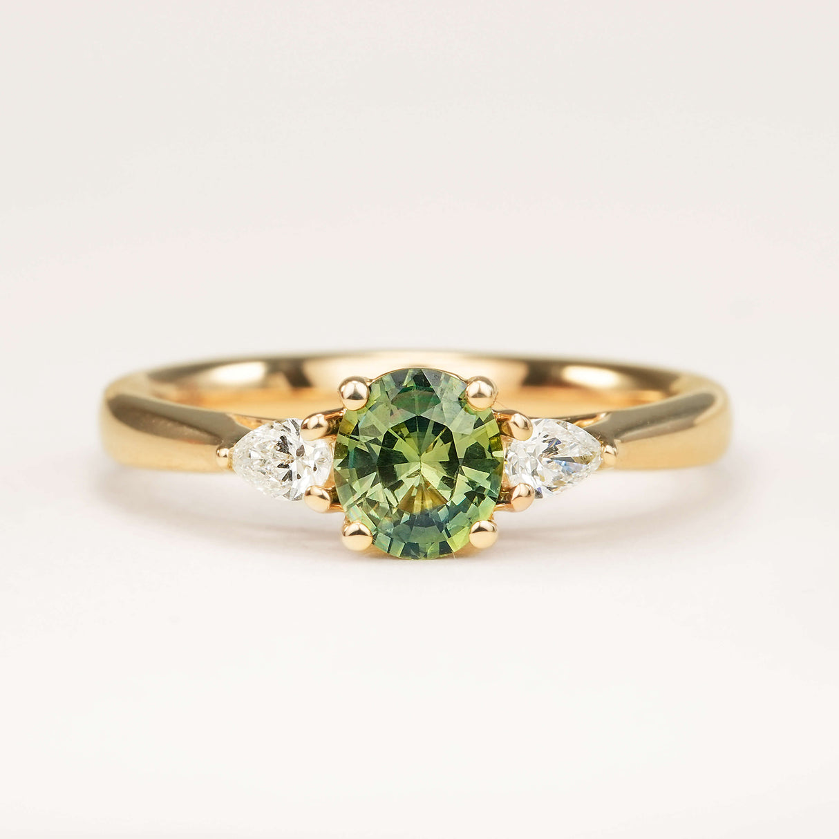 Oval Sri Lankan green sapphire and diamond three-stone wed-fit engagement ring in yellow gold.