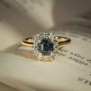 Oval teal sapphire ring with diamond cluster halo setting