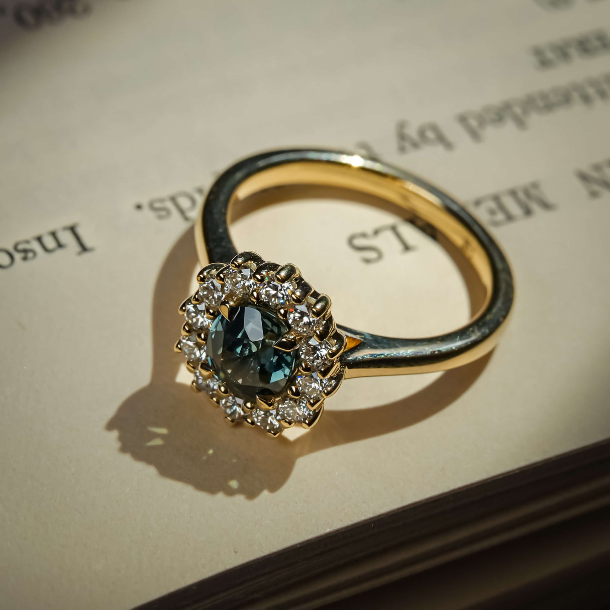 Oval teal sapphire ring with diamond cluster halo setting