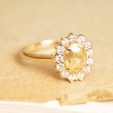Yellow sapphire and diamond cluster engagement ring with oval-cut yellow sapphire and brilliant-cut diamond halo.