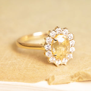 Yellow sapphire and diamond cluster engagement ring with oval-cut yellow sapphire and brilliant-cut diamond halo.