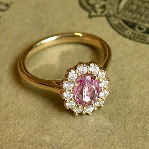Oval padparadscha pink sapphire engagement ring with diamond cluster setting
