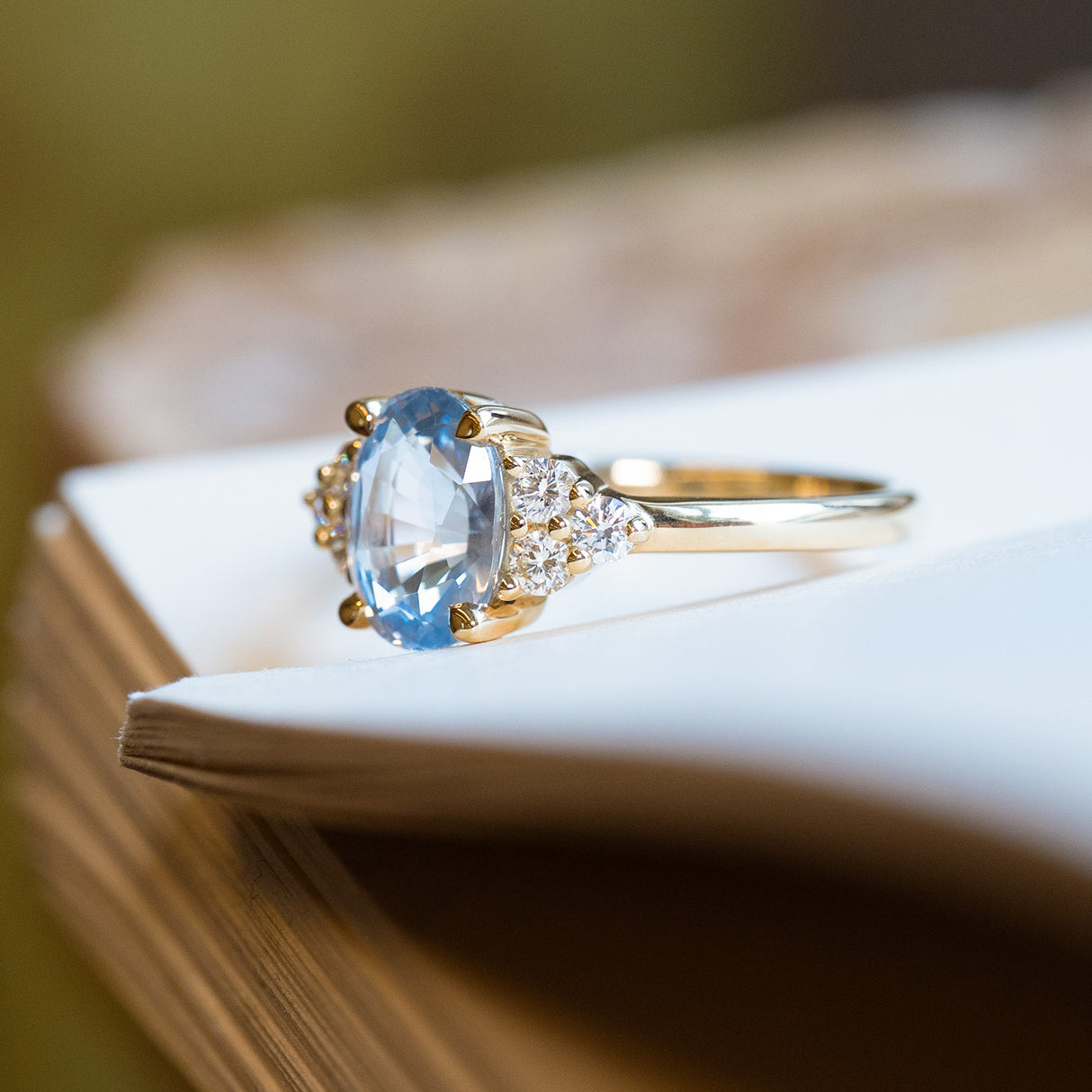Pale blue sapphire and diamond cluster tre-foil engagement ring with diamond-set shoulders and oval sapphire centre.