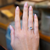 Pale blue sapphire and diamond cluster tre-foil engagement ring worn on hand with oval sapphire centre stone.