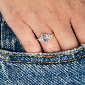 Pale blue sapphire and diamond cluster tre-foil engagement ring worn on hand resting in denim pocket.