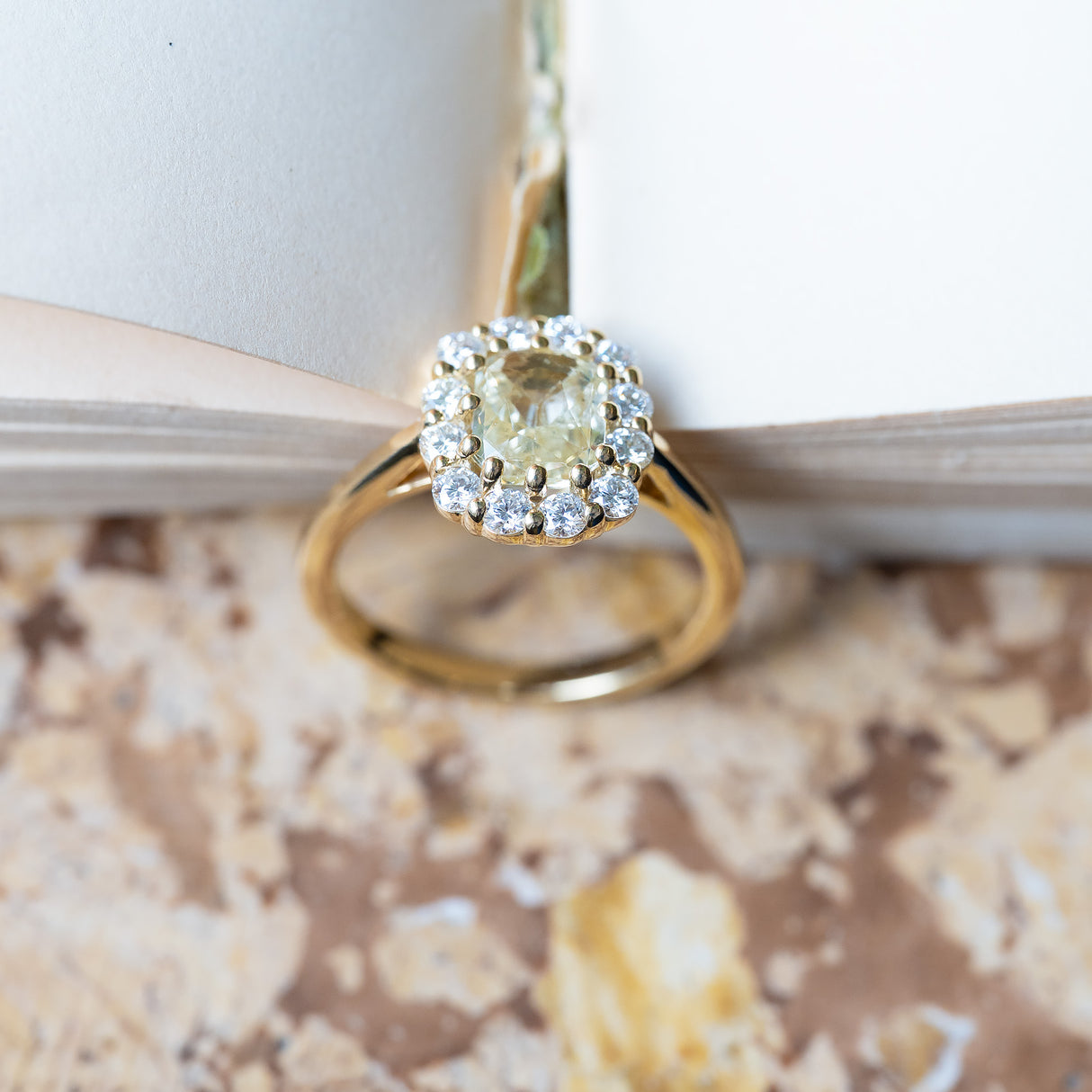 Pale yellow sapphire and diamond cluster engagement ring styled between open book pages.