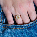 Pale yellow sapphire and diamond cluster engagement ring worn with hand resting in denim pocket.