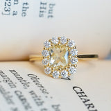 Pale yellow sapphire and diamond cluster engagement ring with surrounding diamond halo on book pages.