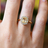 Pale yellow sapphire and diamond cluster engagement ring with diamond halo and gold band.