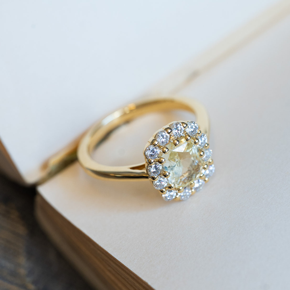 Pale yellow sapphire and diamond cluster engagement ring with polished gold band and diamond halo.