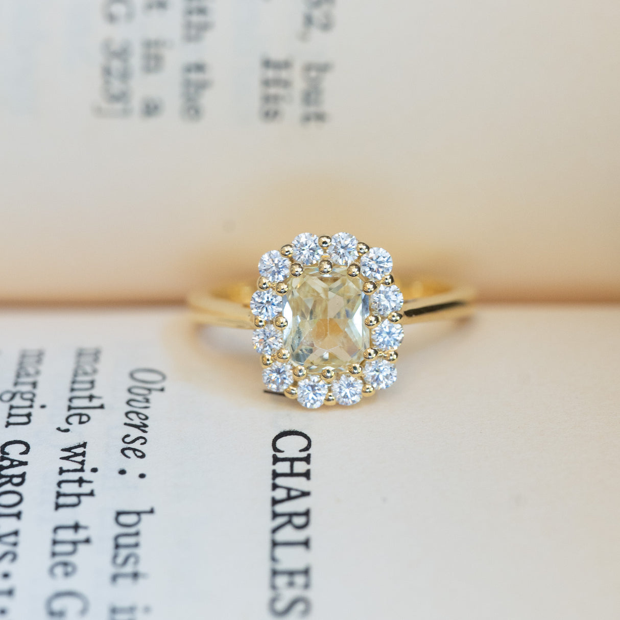 Pale yellow sapphire and diamond cluster engagement ring displayed on vintage book pages.