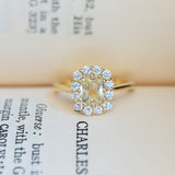 Pale yellow sapphire and diamond cluster engagement ring displayed on vintage book pages.