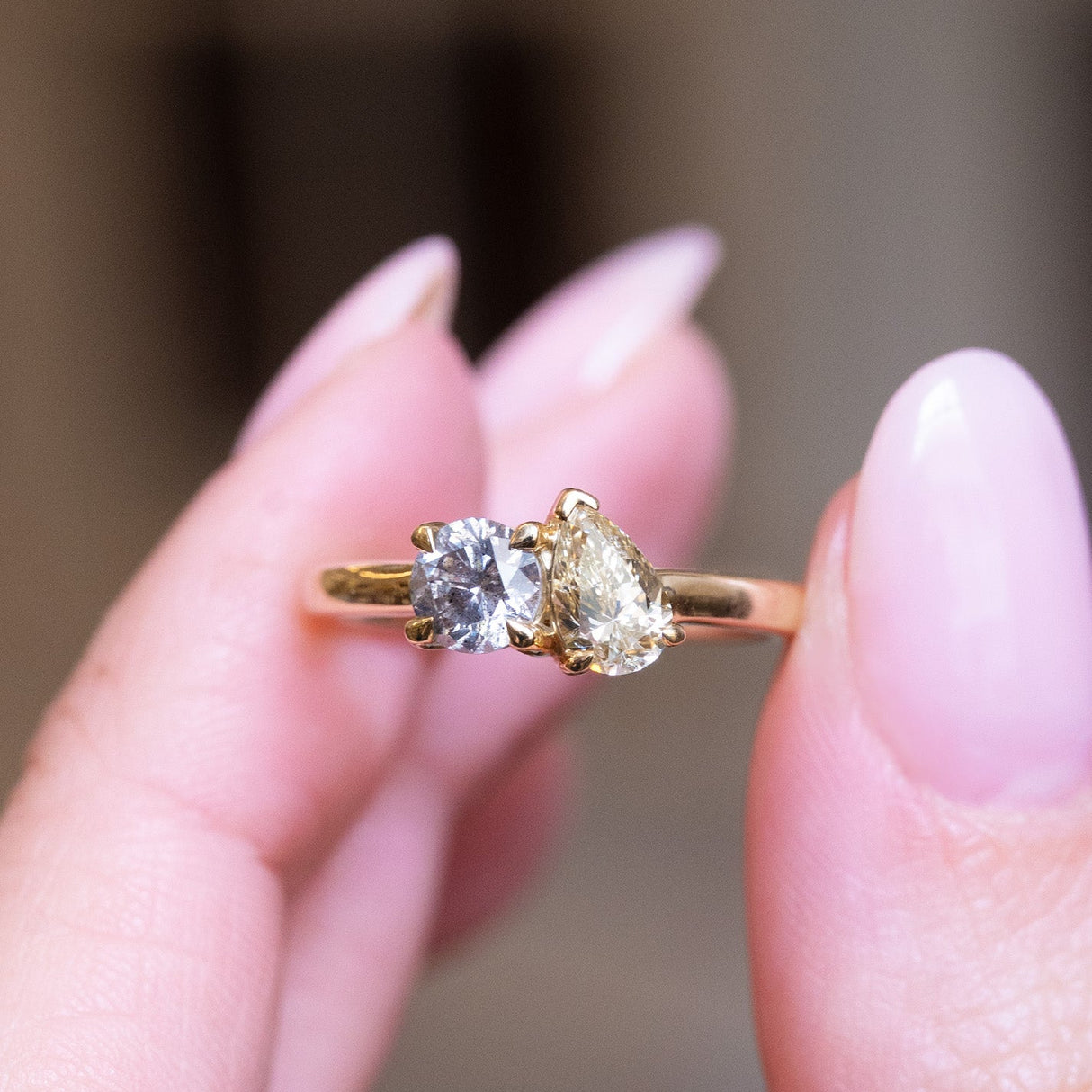 Gold ring with two diamonds held between fingers against a blurred background