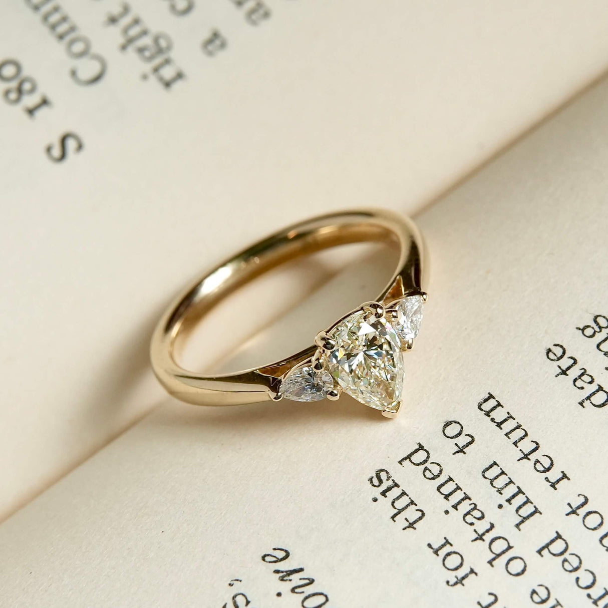 Pear cut diamond three stone engagement ring in yellow gold with diamond side stones
