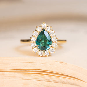 Pear-cut teal tourmaline and diamond cluster engagement ring in yellow gold.