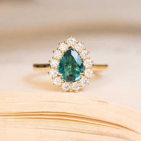 Pear-cut teal tourmaline and diamond cluster engagement ring in yellow gold.