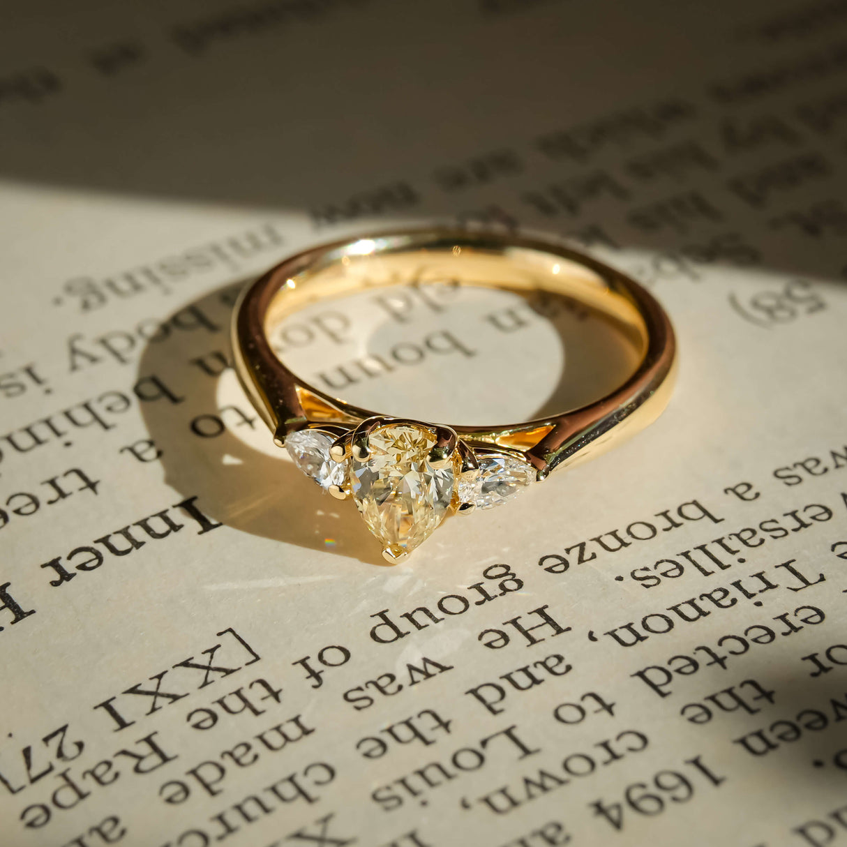 pear cut yellow diamond three stone engagement ring with white diamond side stones in yellow gold