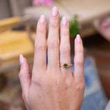 Pine green sapphire and diamond engagement ring worn on hand with gold band.