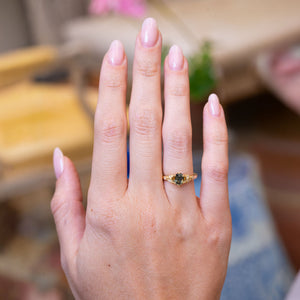 Pine green sapphire and diamond engagement ring worn on hand with gold band.
