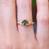 Pine green sapphire and diamond engagement ring with oval-cut centre stone worn on finger.