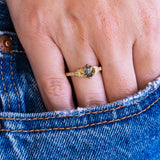 Pine green sapphire and diamond engagement ring worn on hand with denim pocket styling.