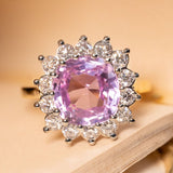 Pink Ceylon sapphire and diamond cluster engagement ring featuring a pastel pink cushion-cut sapphire surrounded by a sparkling halo of round brilliant-cut diamonds.