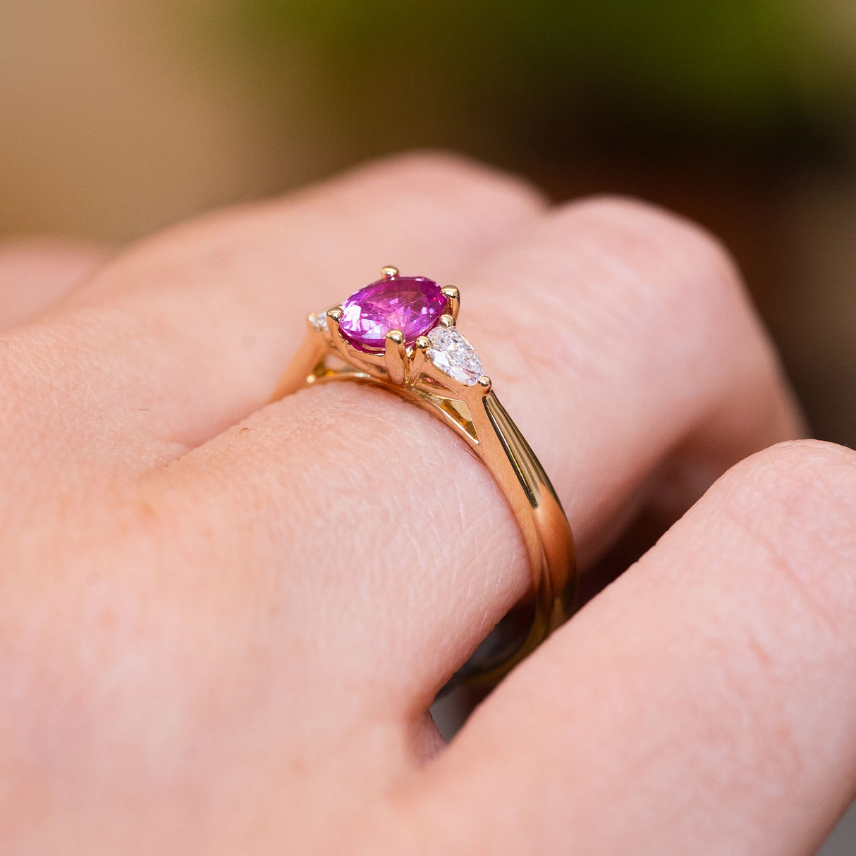 Pink oval sapphire and diamond three-stone engagement ring with gold setting and diamond side stones.