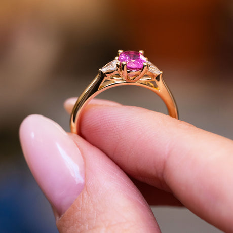 Pink oval sapphire and diamond three-stone engagement ring showing raised gold setting and open gallery.