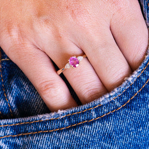 Pink oval sapphire and diamond three-stone engagement ring worn on hand with denim pocket styling.