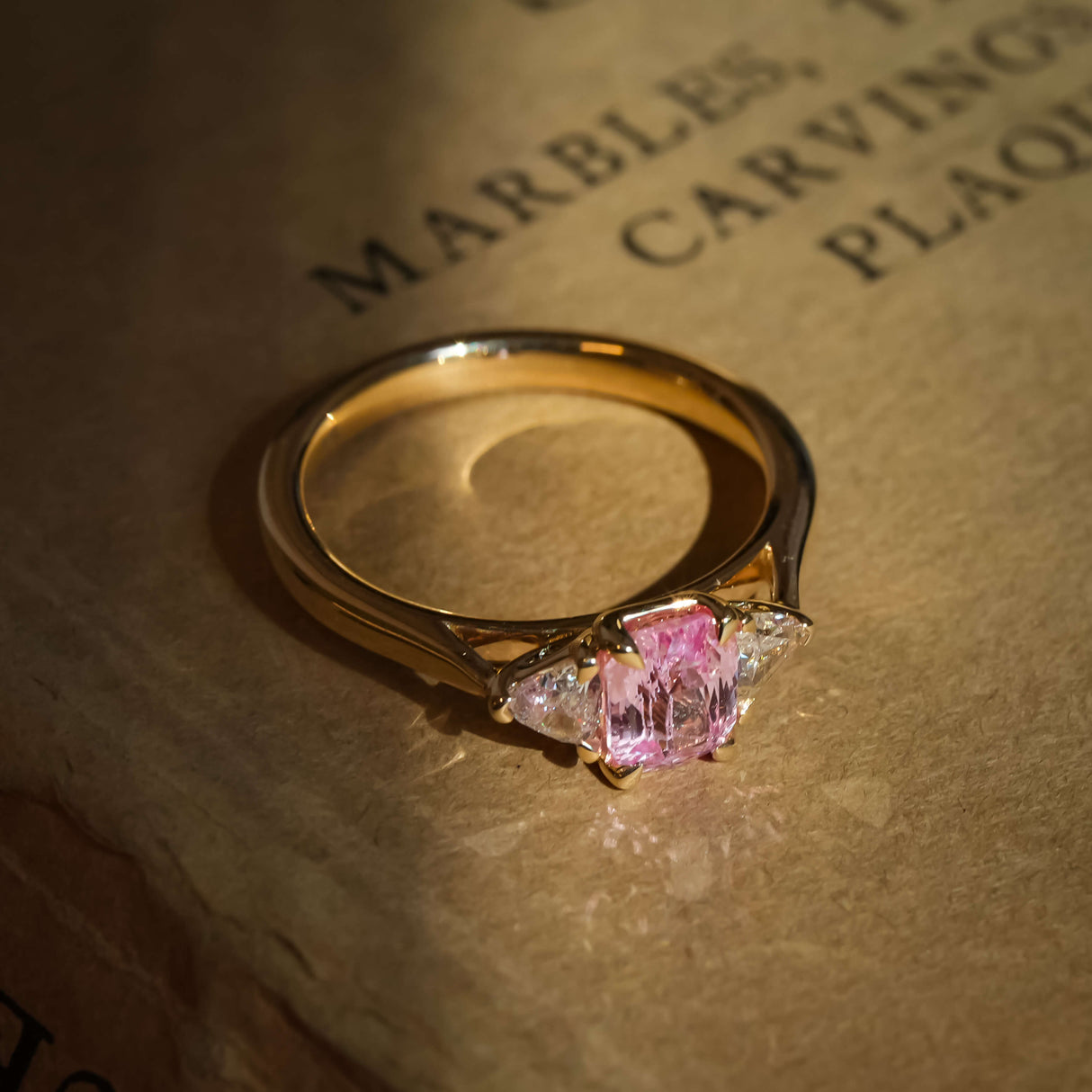 Pink padparadscha sapphire and diamond three stone engagement ring in yellow gold