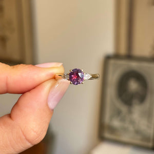 Pink-red sapphire and diamond three-stone engagement ring featuring a round pink-red sapphire centre stone with pear-cut diamond side stones, held by hand.