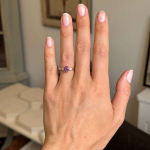 Pink-red sapphire and diamond three-stone engagement ring with a round pink-red sapphire and pear-cut diamond accents, displayed on a hand.