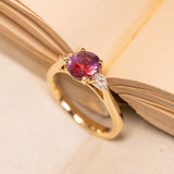 Three-stone engagement ring showcasing a richly coloured pink-red sapphire framed by pear-cut diamonds in a classic yellow gold setting.