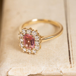 Antique-inspired pink sapphire and diamond cluster engagement ring featuring a sunset pink sapphire and brilliant-cut diamond halo in yellow gold.