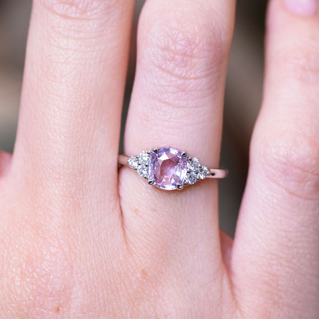 Pink sapphire and diamond cluster tre-foil engagement ring with oval pink sapphire and diamond detailing worn on finger.
